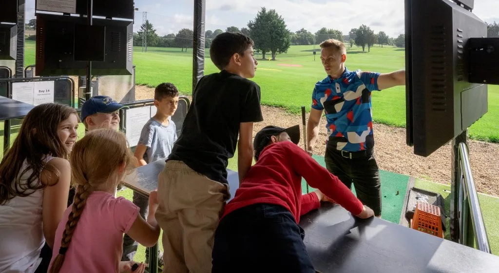 A golf instructor teaching a junior group lesson on the driving range at Wycombe Heights Golf Club in High Wycombe